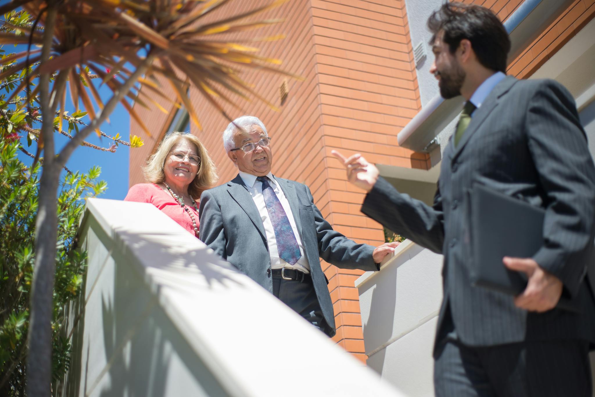 Elderly couple touring a modern home with a real estate agent in sunny Portugal.